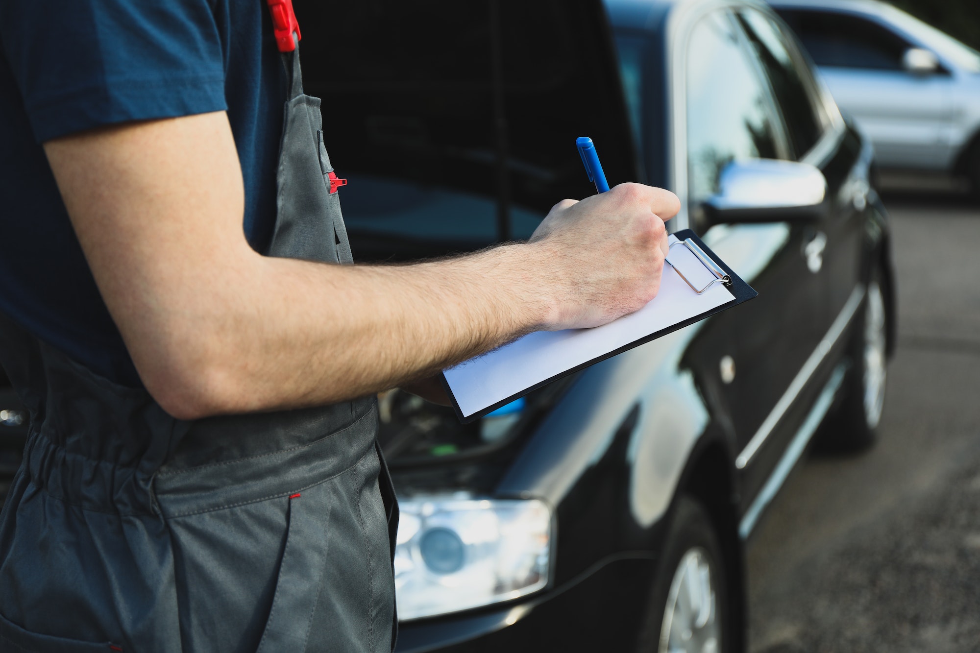 A man in overalls writes to a clipboard. Mechanic. Car inspection